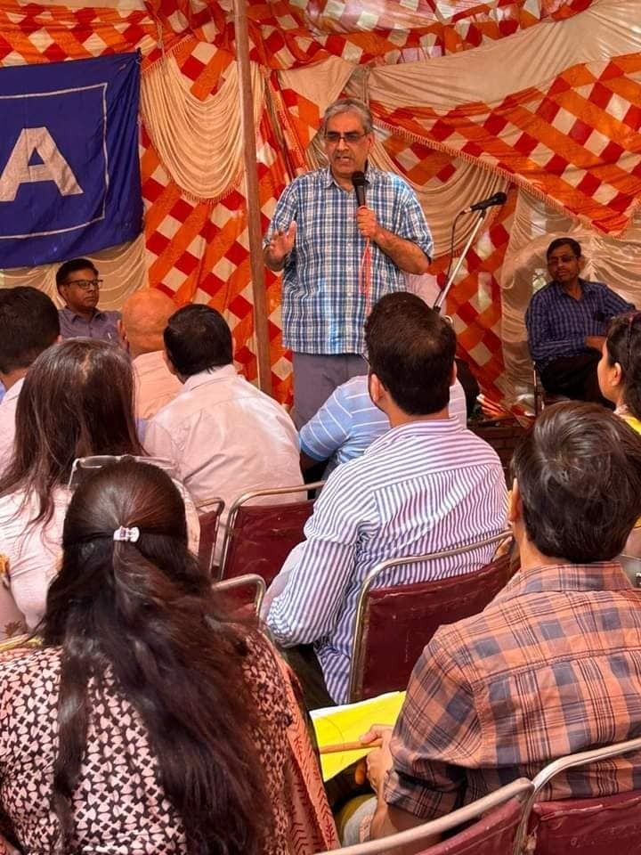 A speaker addresses teachers seated under a canopy at a DUTA meeting